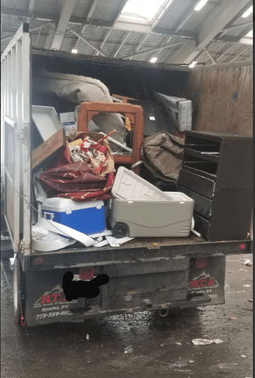 Dump truck bed filled with assorted trash and discarded items.