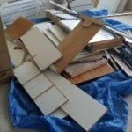 Pile of discarded construction materials: tiles, wood, and metal, on a blue tarp.