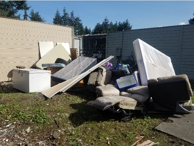 Pile of discarded furniture and debris in a yard; mattresses, cushions, and a cooler.