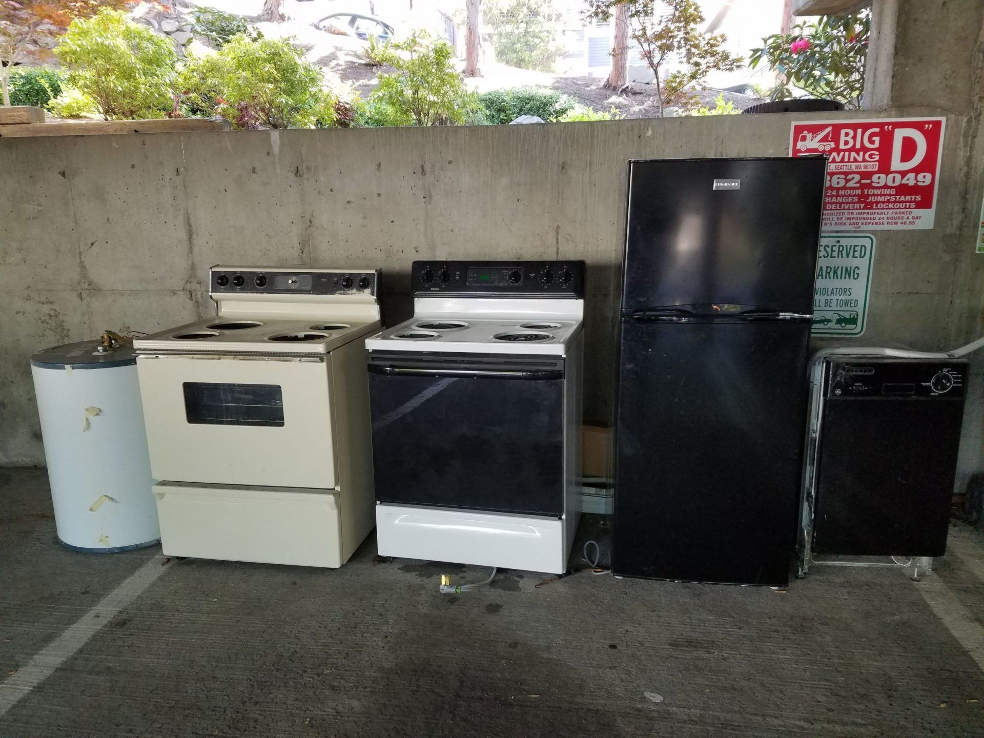 Appliances lined up in a parking space: water heater, two stoves, refrigerator, and dishwasher.
