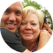 Person hugs woman, both smile. The woman has short blonde hair, outdoors.