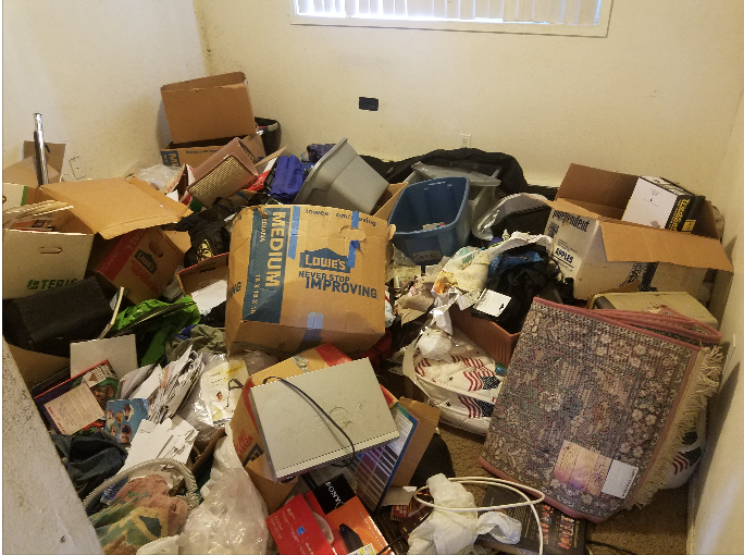 Room filled with clutter: boxes, clothes, and various items scattered on the floor.