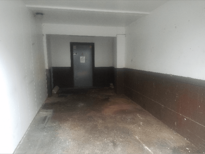 A dimly lit hallway with white and brown walls, leading to a closed gray door.