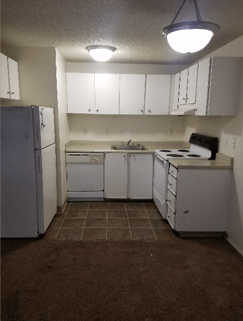 White kitchen with appliances, cabinets, and brown tile and carpet flooring.
