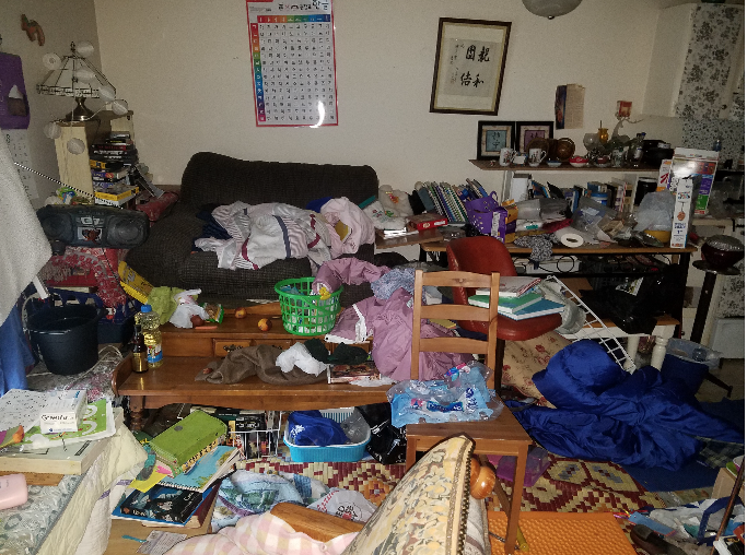 Messy living room with scattered items on furniture and floor.