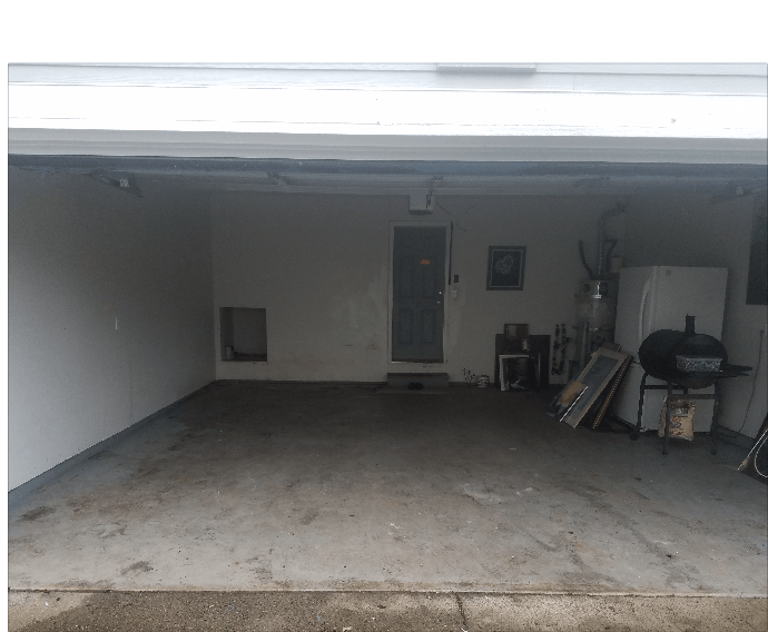 An open garage interior with a concrete floor, a door, and miscellaneous items on the right side.